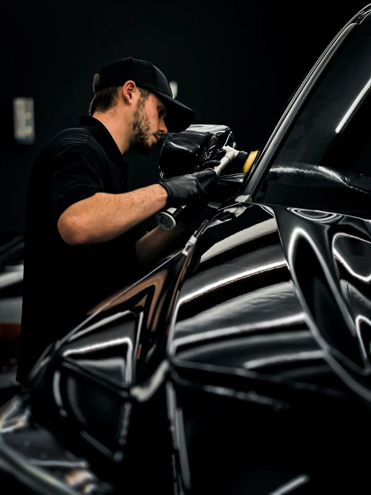 A detailer machine-polishing the wing of a black car